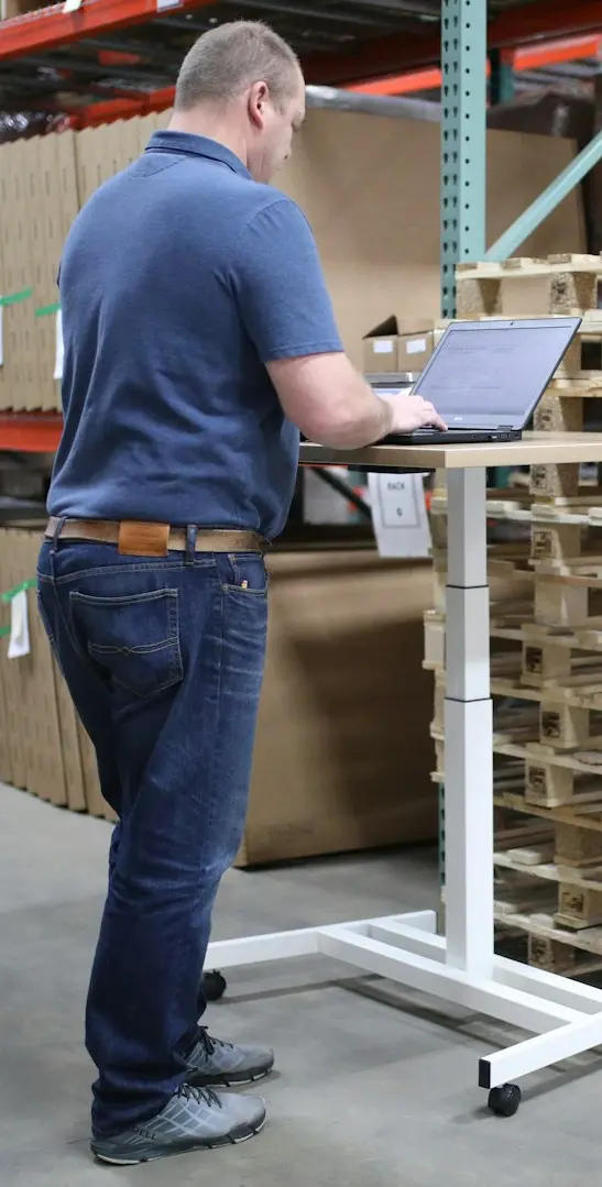 man in blue polo shirt and blue denim jeans standing near brown wooden shelf